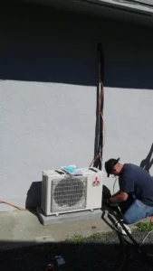 HVAC Blog 1 Technician working on an outdoor air conditioning unit against a gray wall.